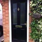 Black GRP Composite front door with a white uPVC outerframe and gold furniture